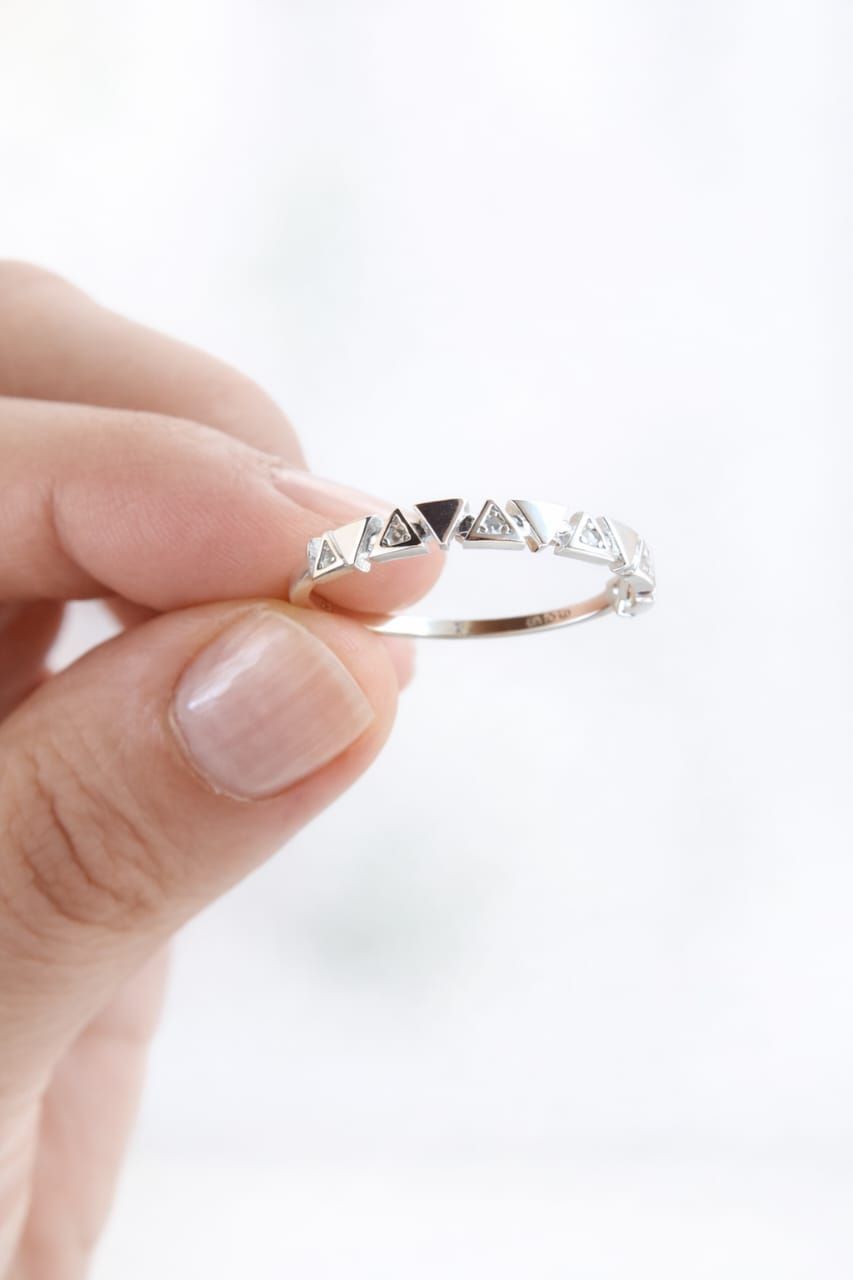 Una mano sosteniendo un anillo de plata con pequeñas piedras transparentes sobre un fondo blanco.