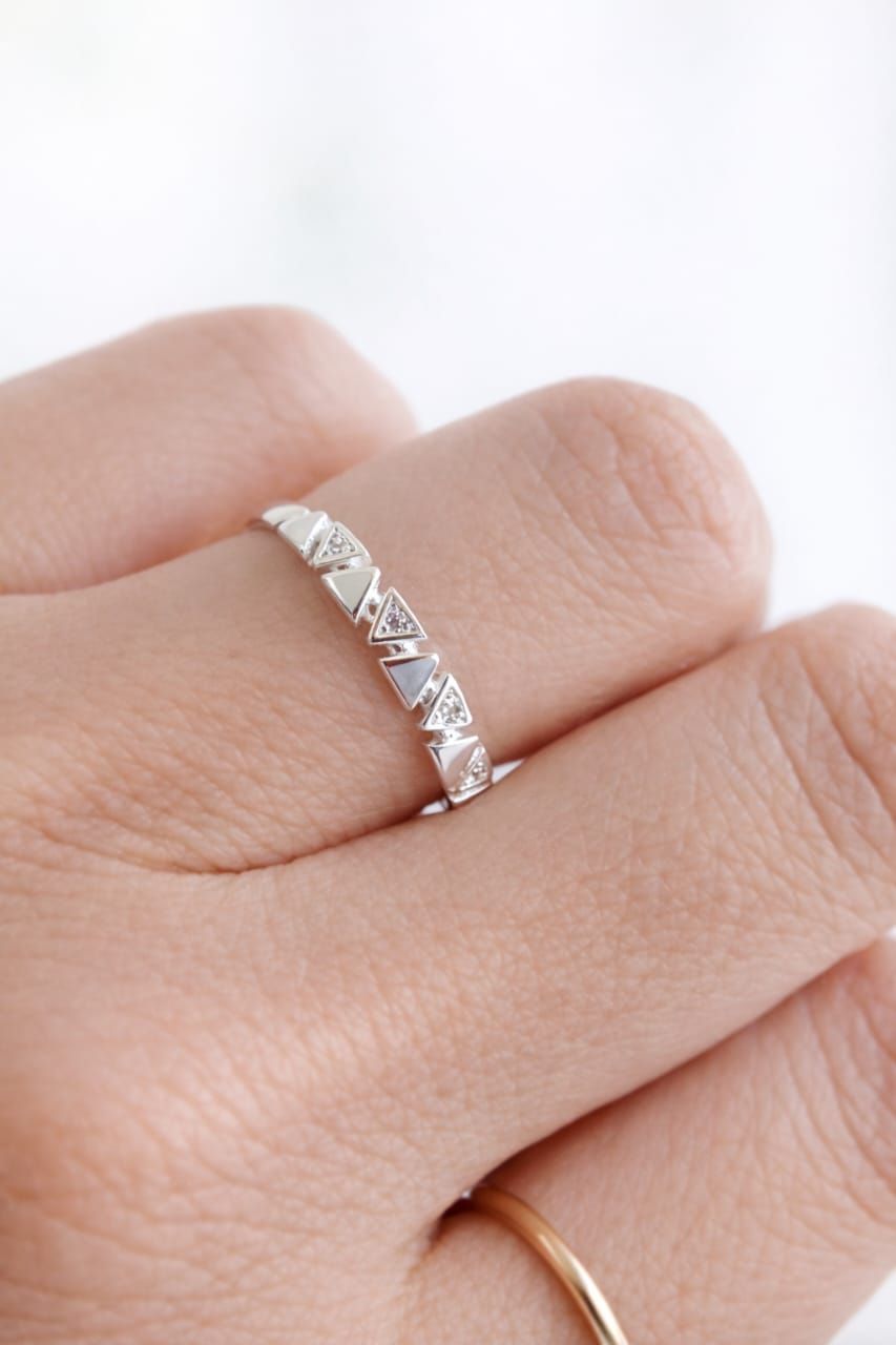 Una mano sosteniendo un anillo de plata con pequeñas piedras transparentes sobre un fondo blanco.