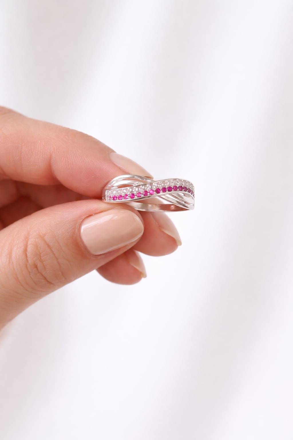 Mano que lleva un anillo de plata con piedras rosas en un dedo.