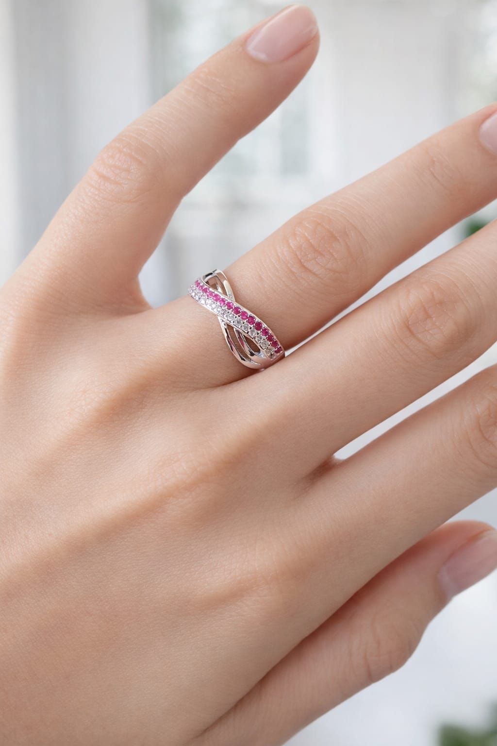 Mano que lleva un anillo de plata con piedras rosas en un dedo.