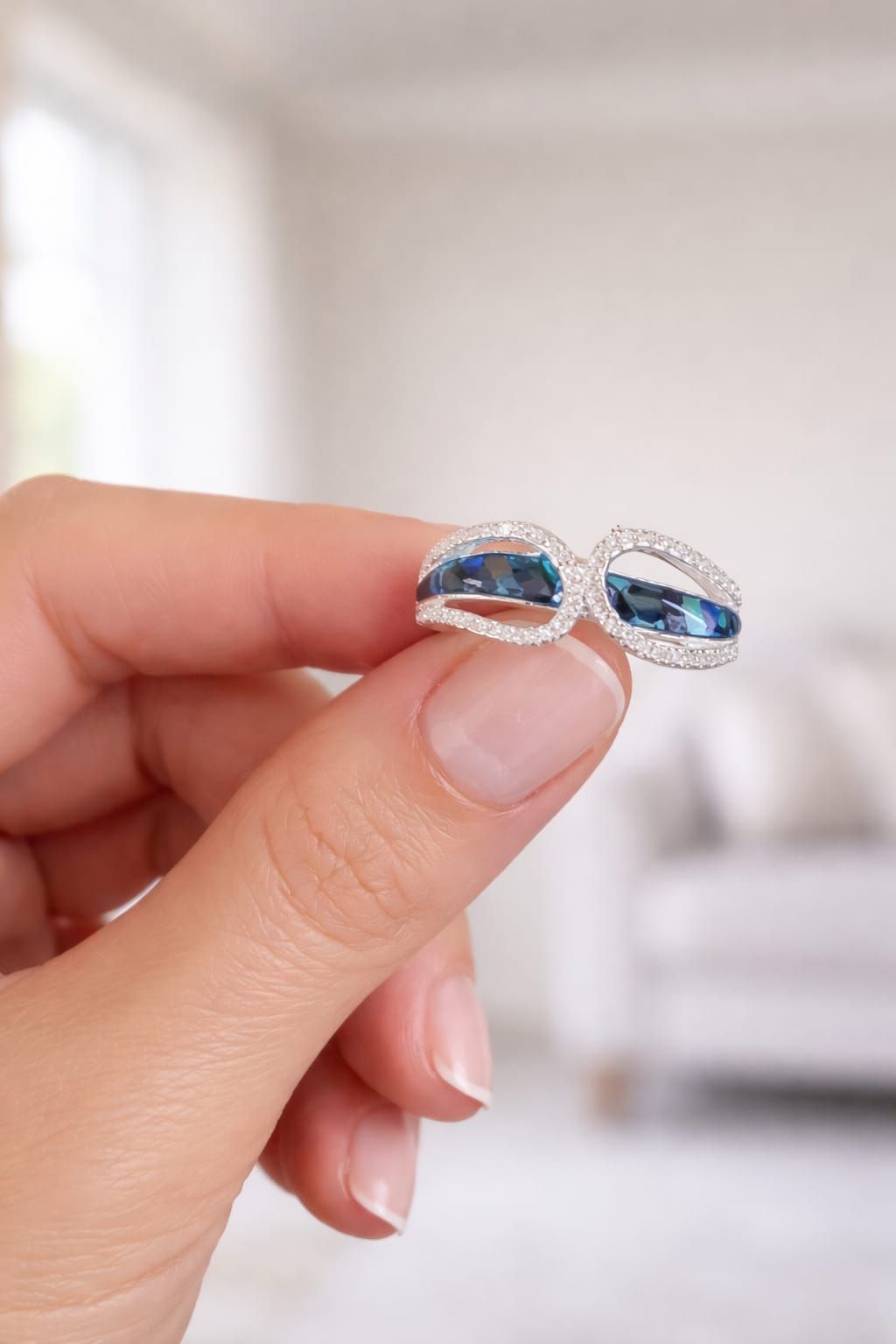 Mano con un anillo de plata con piedras ovaladas azules sobre un fondo suave y desenfocado.