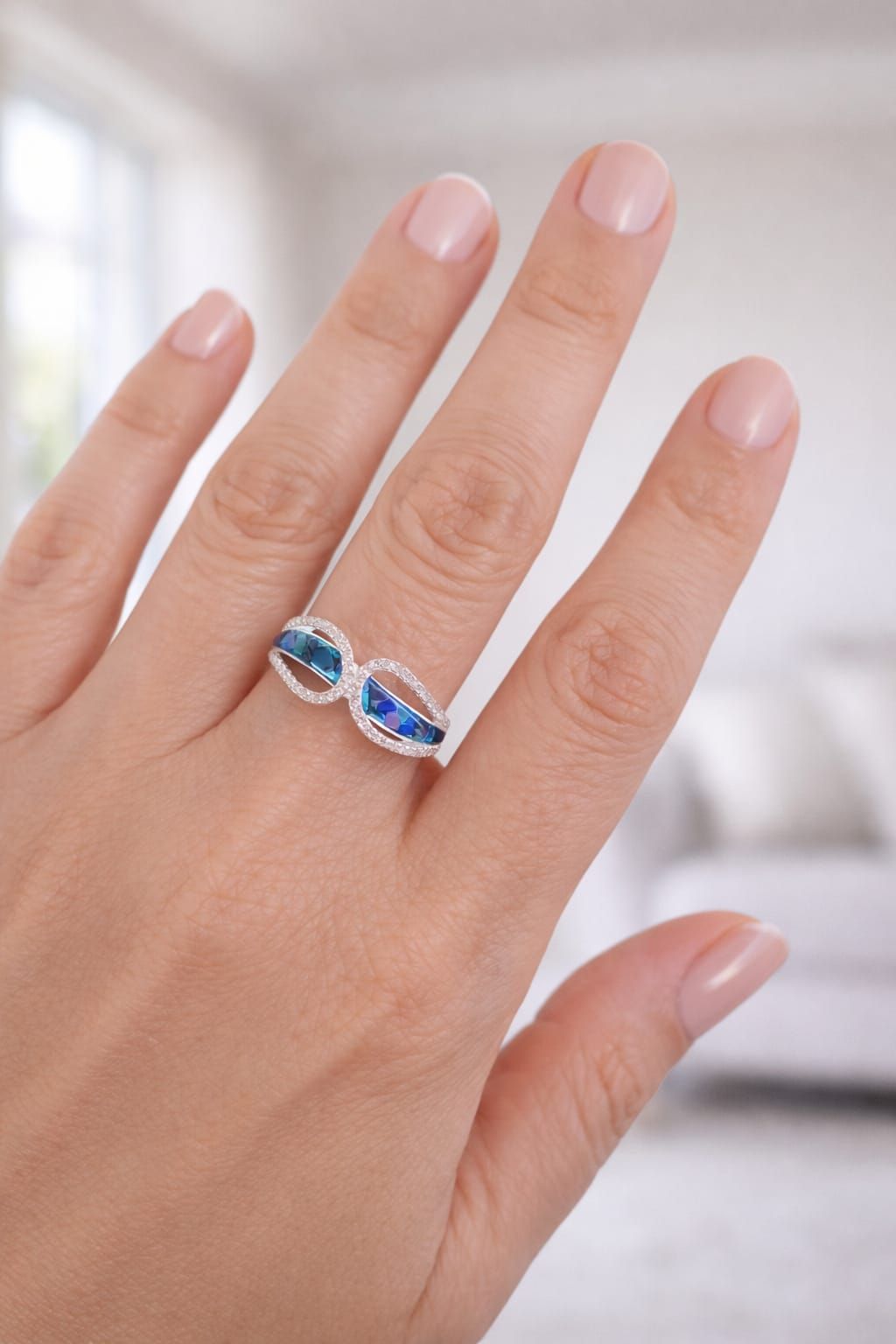 Mano con un anillo de plata con piedras ovaladas azules sobre un fondo suave y desenfocado.
