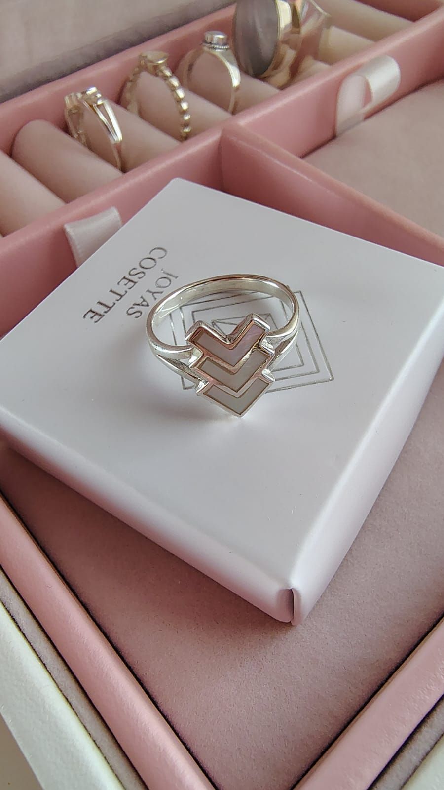 Mano con un anillo plateado en zigzag sobre un fondo neutro.