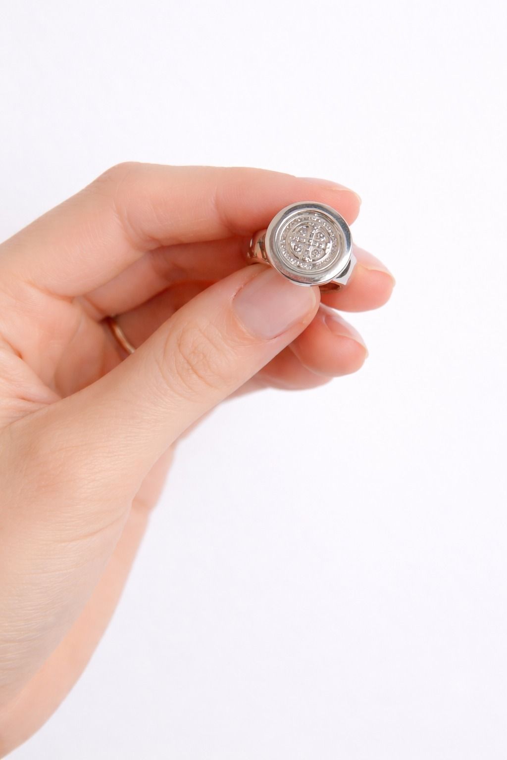 Una mano sosteniendo una pequeña moneda de plata sobre un fondo blanco.