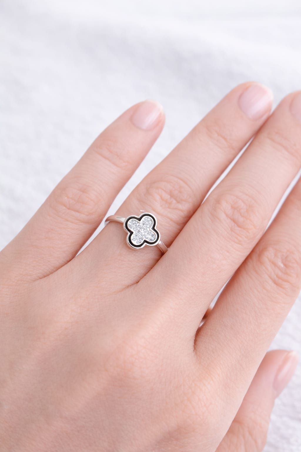 Mano con un anillo de plata con forma de flor de cuatro pétalos sobre un fondo de tela blanca.