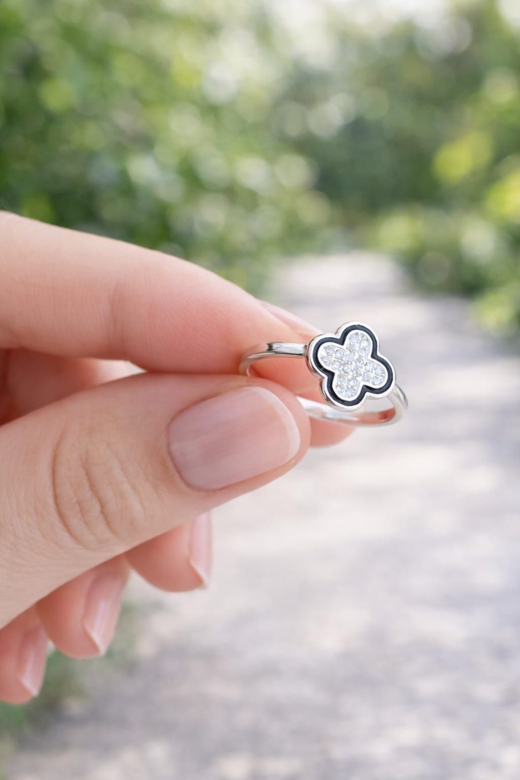 Mano con un anillo de plata con forma de flor de cuatro pétalos sobre un fondo de tela blanca.