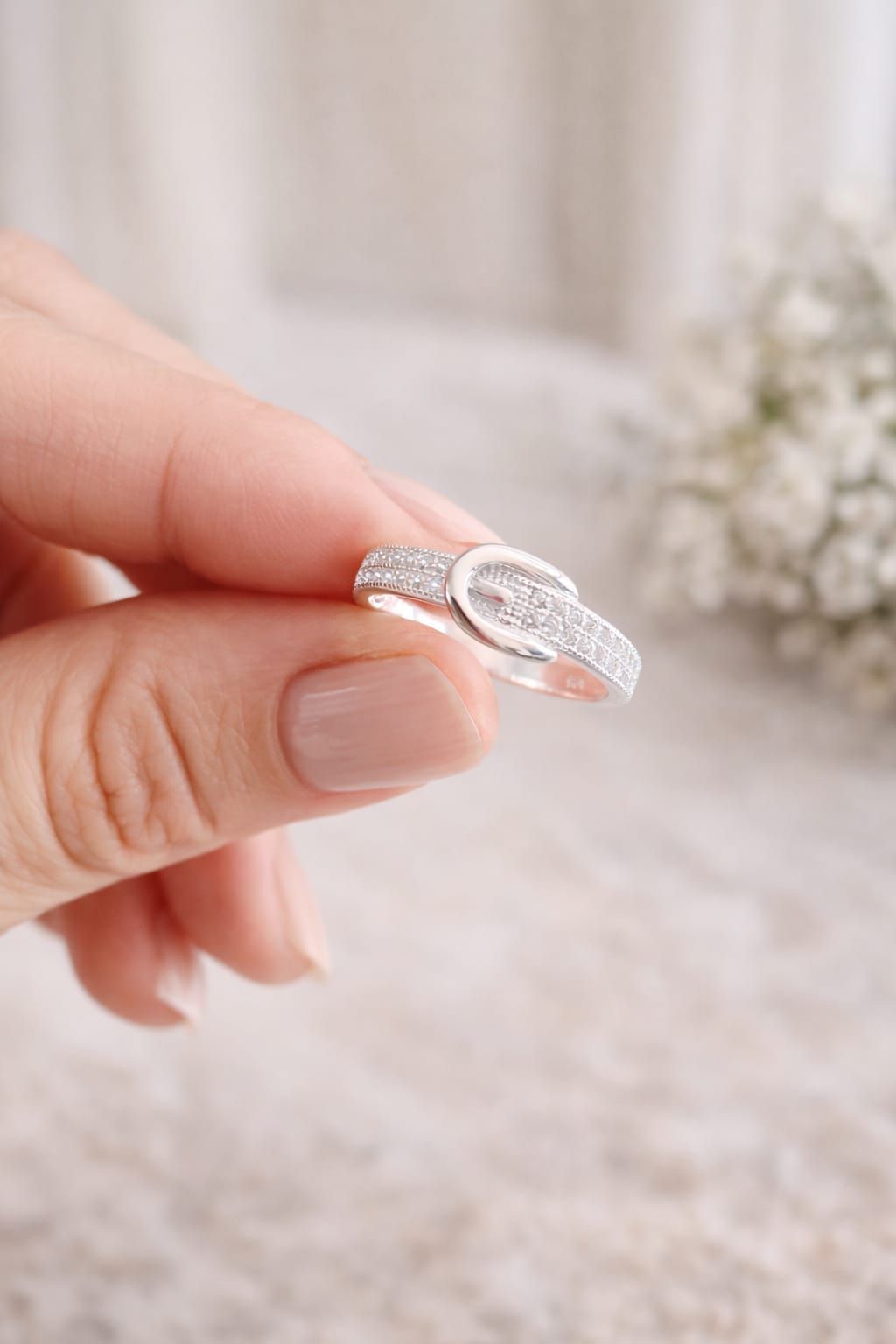 Mano que lleva un anillo ovalado de plata con pequeñas piedras.