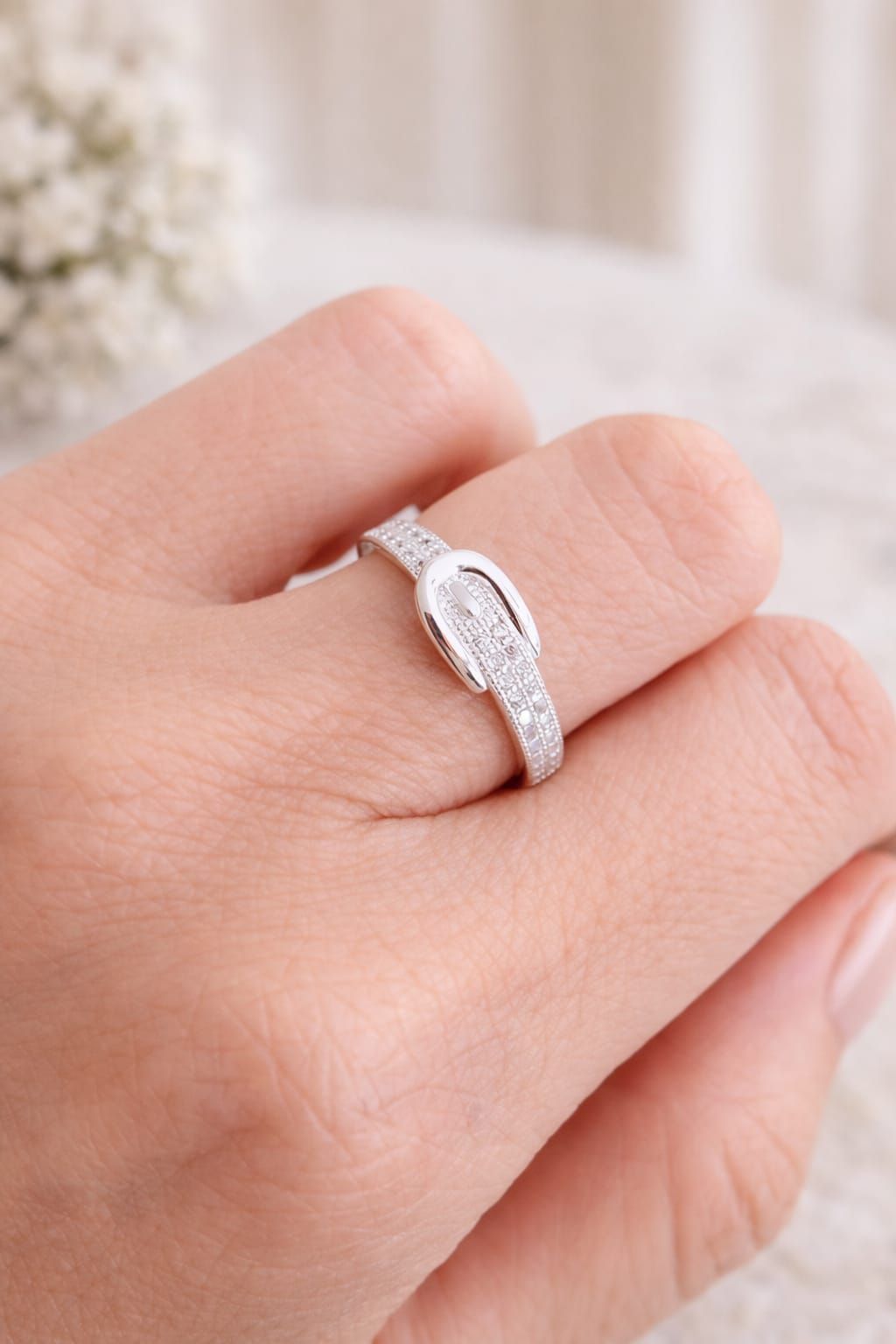 Mano que lleva un anillo ovalado de plata con pequeñas piedras.