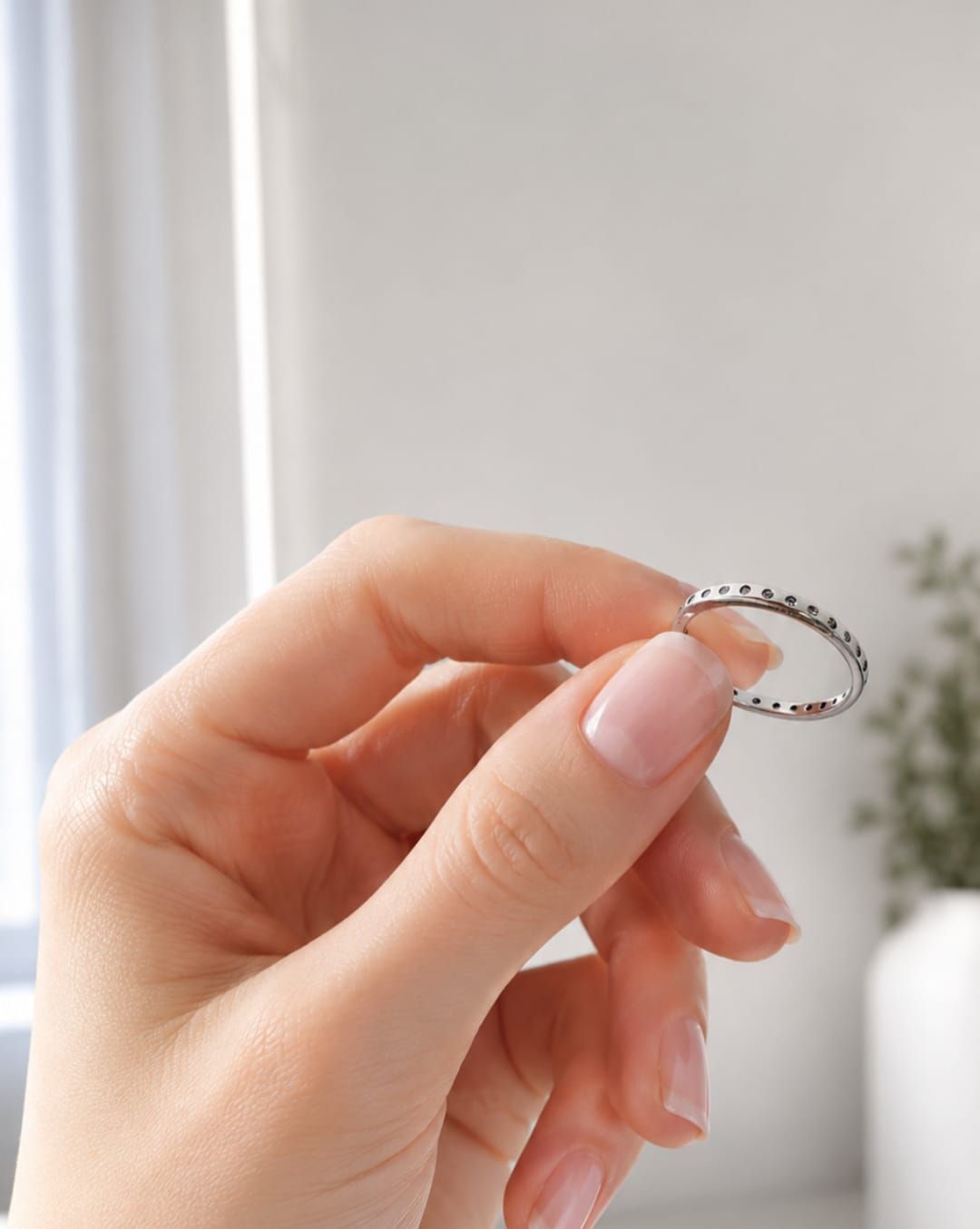 Primer plano de una mano que lleva dos anillos de plata con pequeñas piedras, apoyada sobre una superficie blanca.