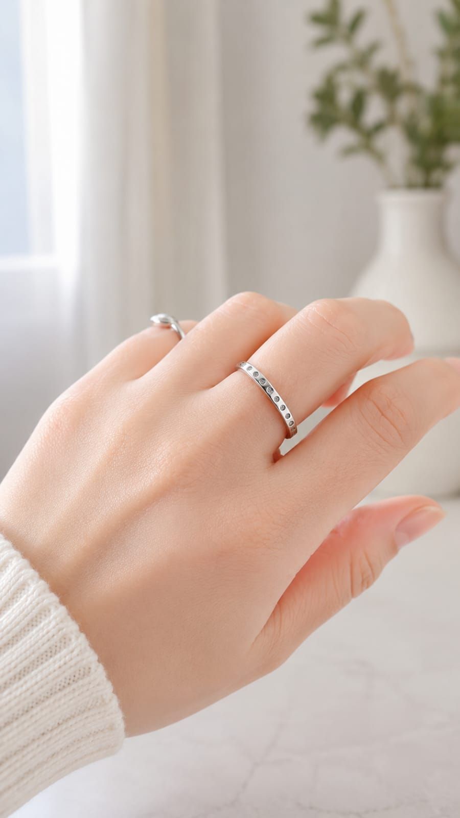 Primer plano de una mano que lleva dos anillos de plata con pequeñas piedras, apoyada sobre una superficie blanca.