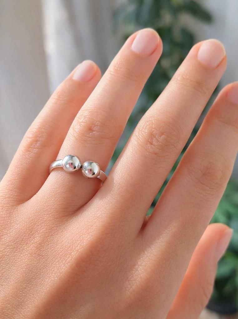 Una mano con un anillo de plata y una piedra preciosa transparente descansa sobre un fondo suavemente difuminado.
