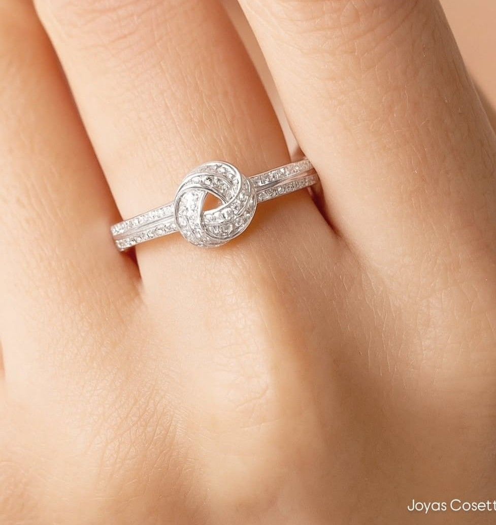 Primer plano de un anillo de plata con diamantes en un dedo, con una piedra central redonda.