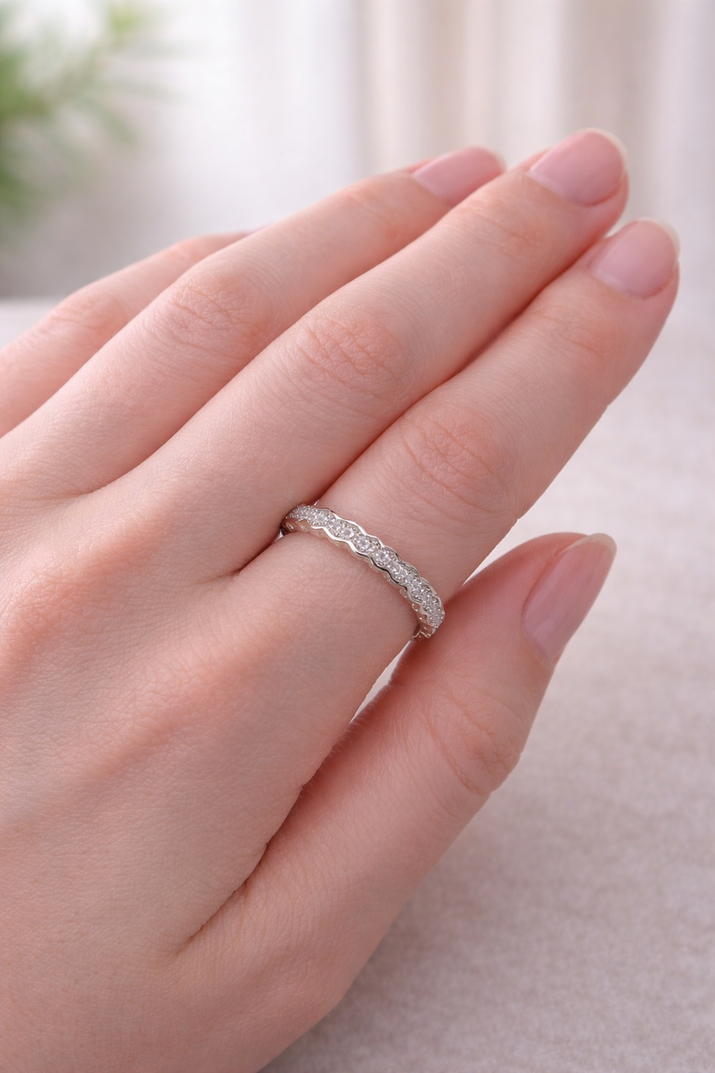Mano con un anillo de plata adornado con pequeñas piedras transparentes en el dedo anular.
