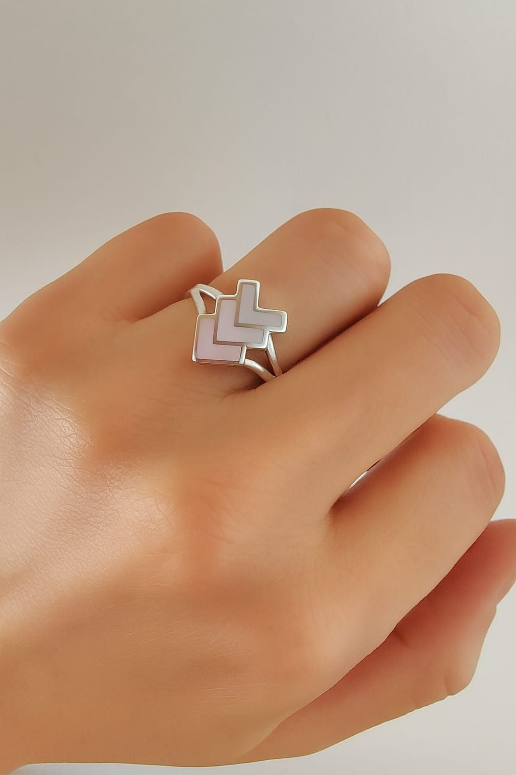 Mano con un anillo plateado en zigzag sobre un fondo neutro.