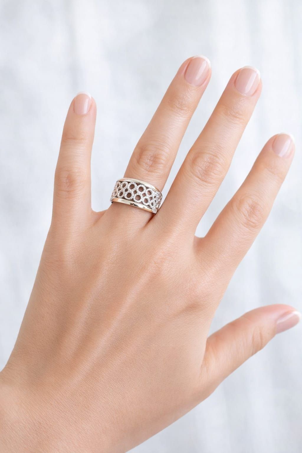 Mano con un anillo de rejilla de plata sobre fondo claro