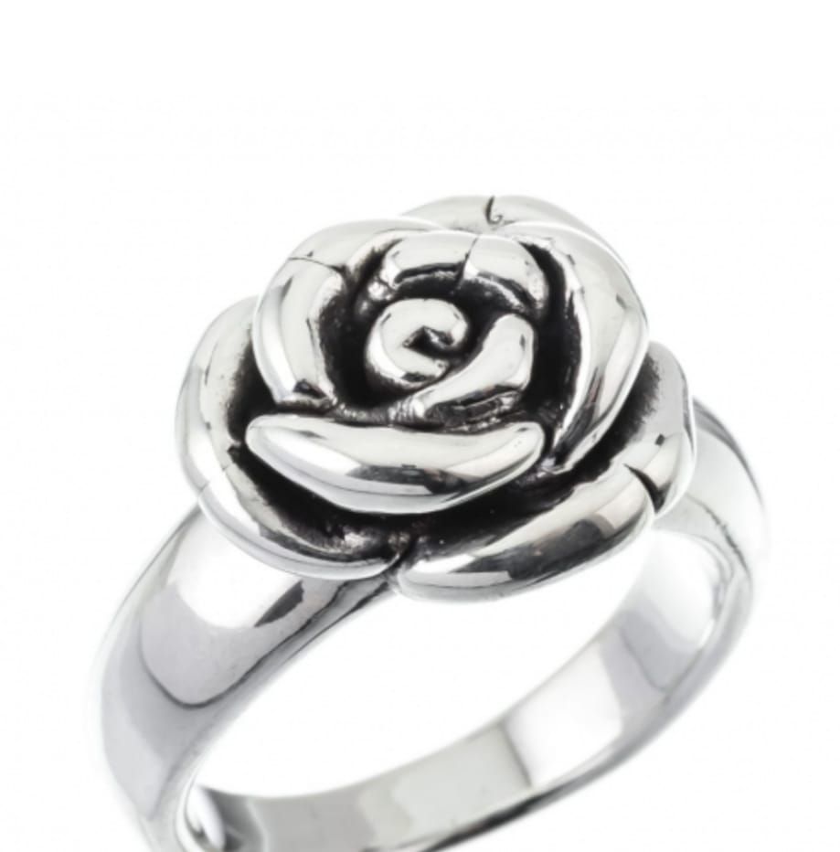 Mano con un anillo plateado en forma de flor sobre un fondo blanco.