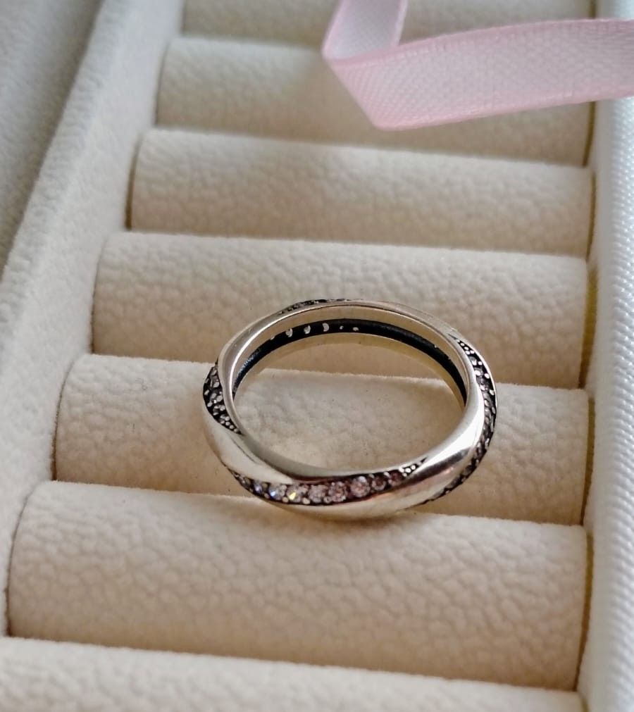 Dos anillos de plata con pequeñas piedras que reposan en un estuche para anillos de color crema.