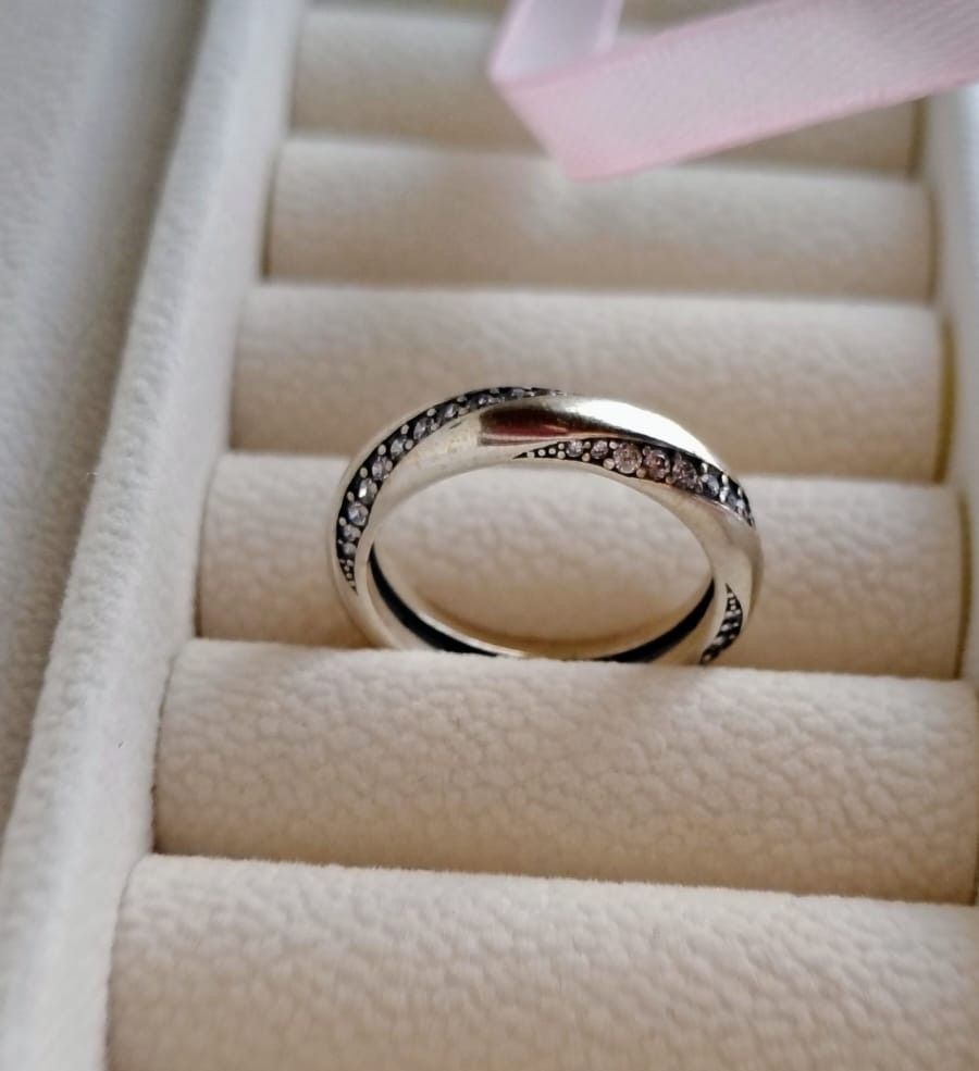 Dos anillos de plata con pequeñas piedras que reposan en un estuche para anillos de color crema.