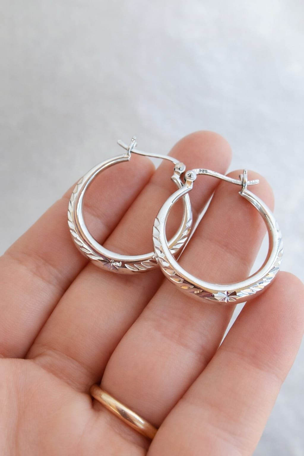 Una mano sosteniendo dos anillos de plata en el fondo borroso de una sala de estar.