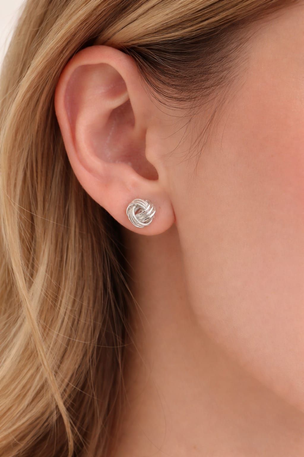 Primer plano de la oreja de una persona que lleva un pequeño pendiente de plata con una gema transparente.