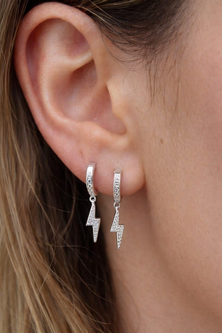 Primer plano de una oreja con pendientes colgantes de plata en forma de rayo.