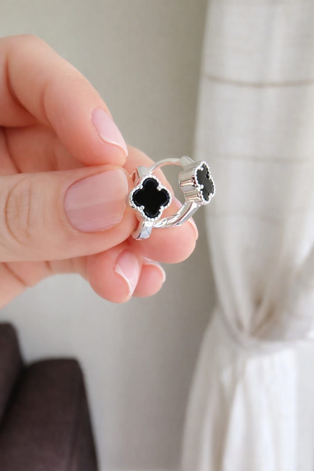 Mano sosteniendo un anillo de plata con un diseño de trébol de cuatro hojas negro, sobre un fondo suave de interior.