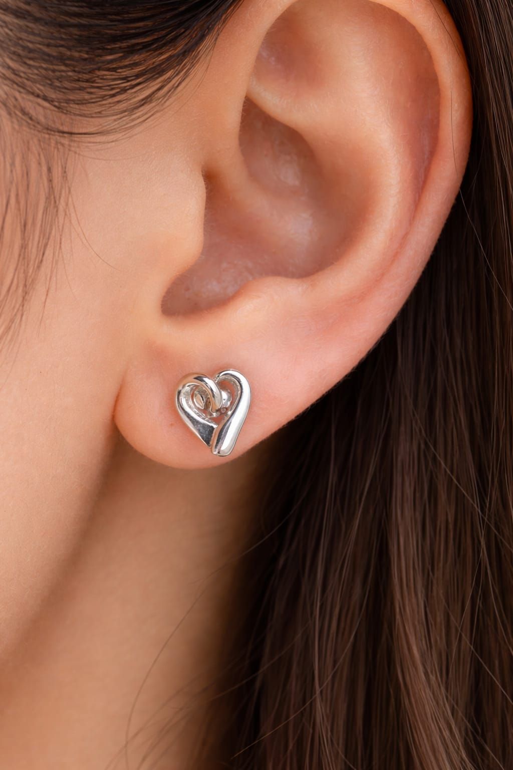 Primer plano de una oreja con un pendiente de plata en forma de corazón con una gema transparente.