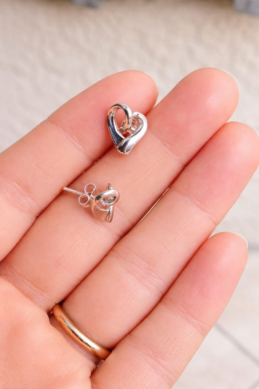 Primer plano de una oreja con un pendiente de plata en forma de corazón con una gema transparente.