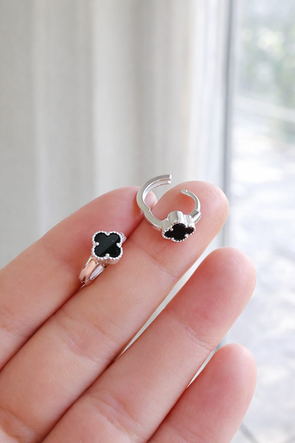 Mano sosteniendo un anillo de plata con un diseño de trébol de cuatro hojas negro, sobre un fondo suave de interior.