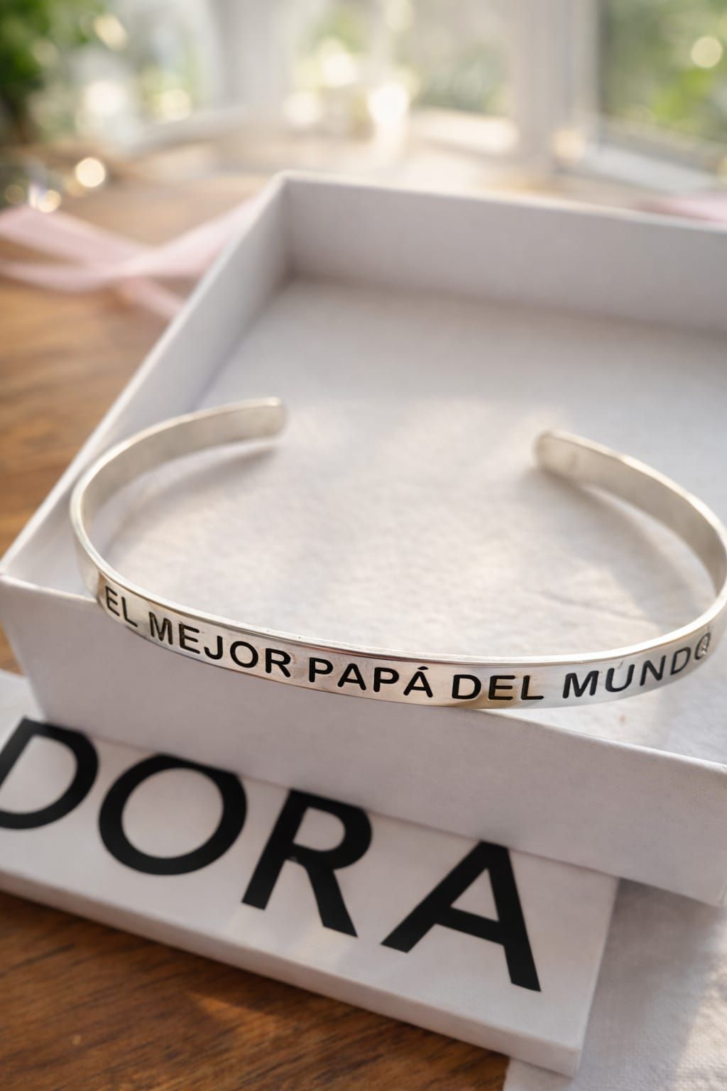 White gift box with a silver “EL MEJOR PAPÁ DEL MUNDO” bracelet on a table