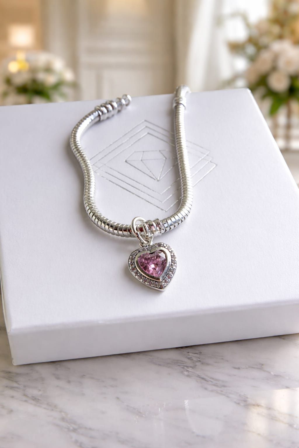 Collar de cadena plateada con colgante de corazón rosa en una caja blanca.