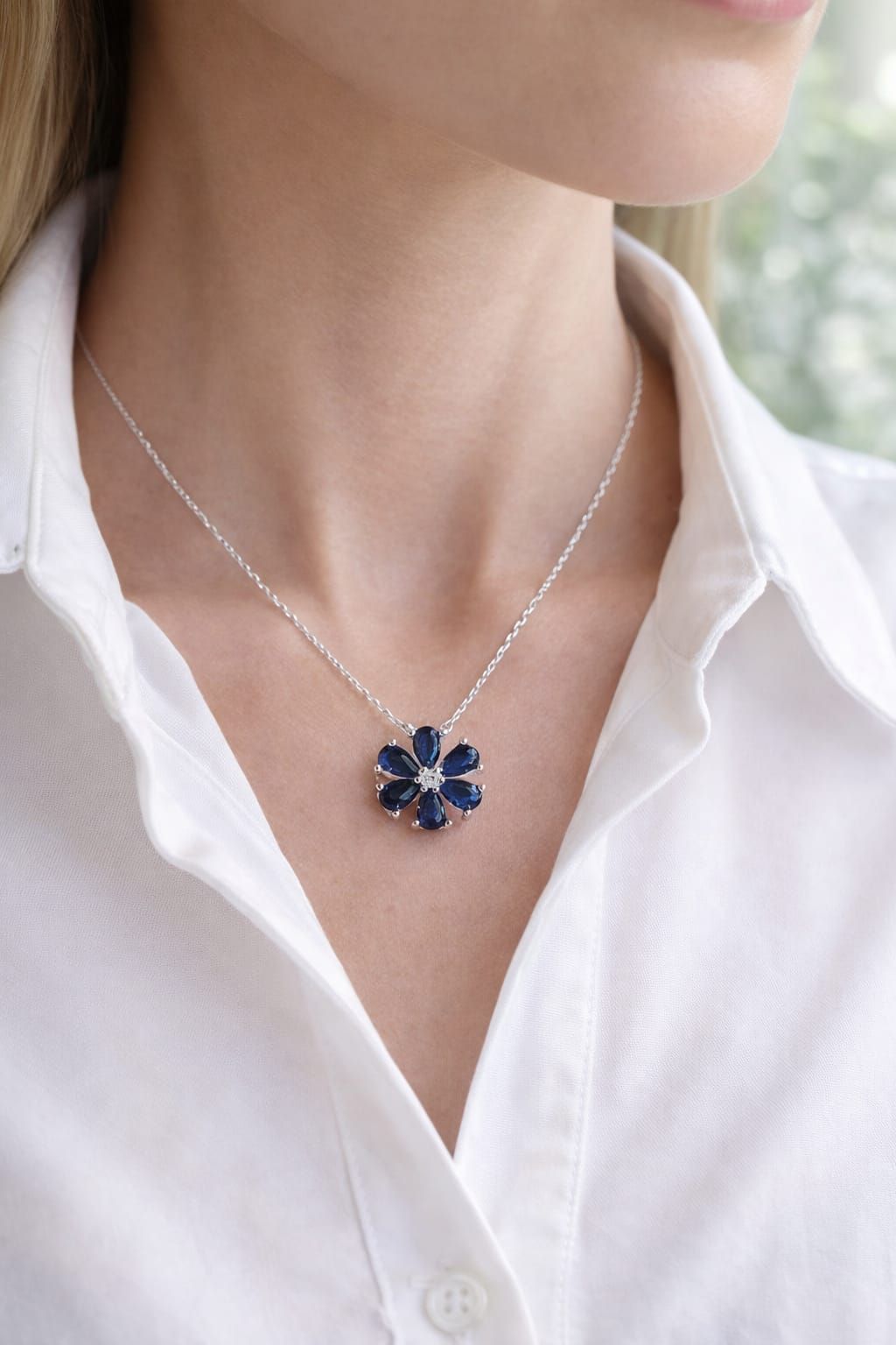 Primer plano de un collar de plata con un colgante de flor azul marino sobre una blusa blanca.