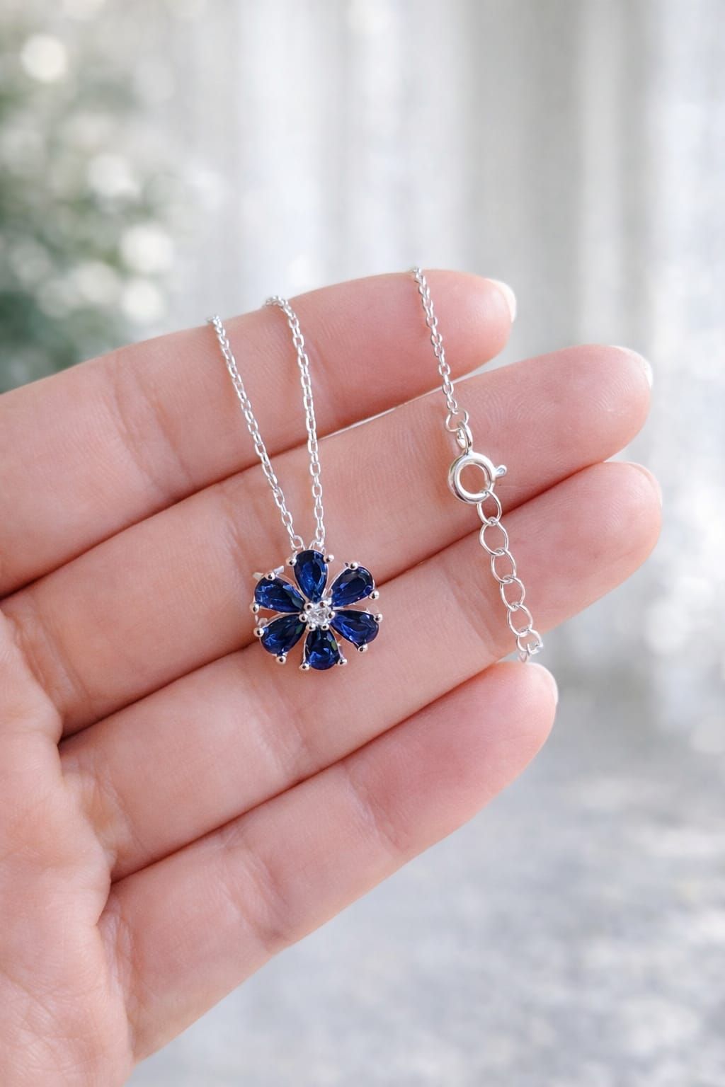 Primer plano de un collar de plata con un colgante de flor azul marino sobre una blusa blanca.