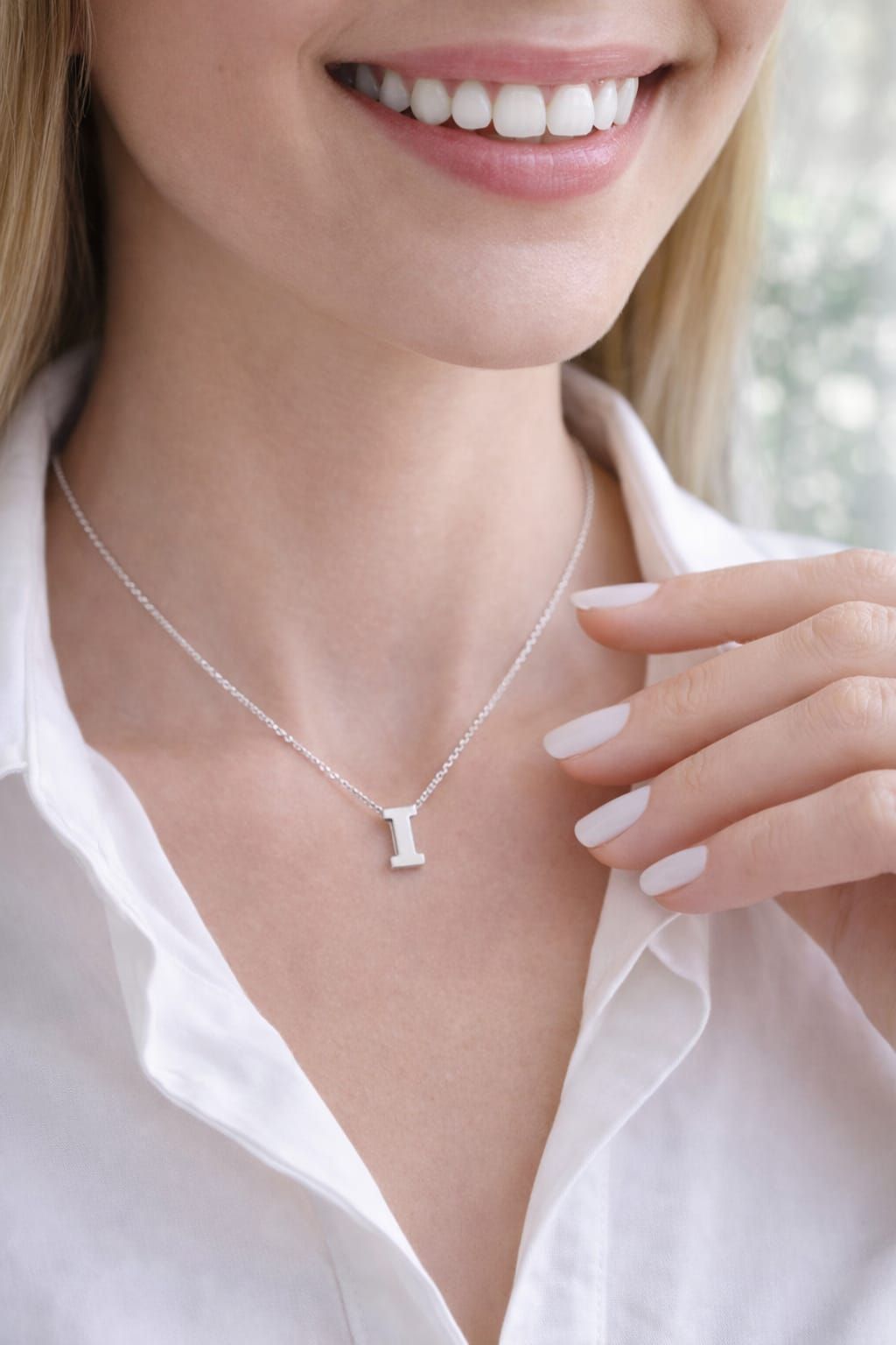 Primer plano de una persona sonriente que lleva un collar de plata con un colgante y una camisa blanca.