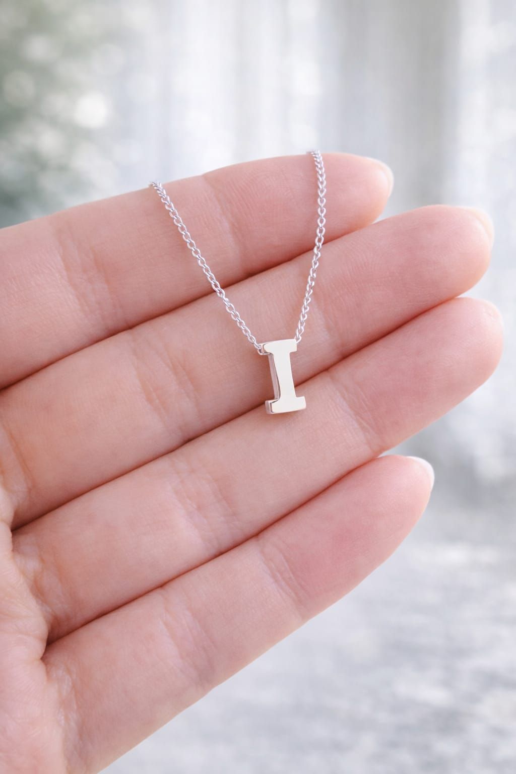Primer plano de una persona sonriente que lleva un collar de plata con un colgante y una camisa blanca.