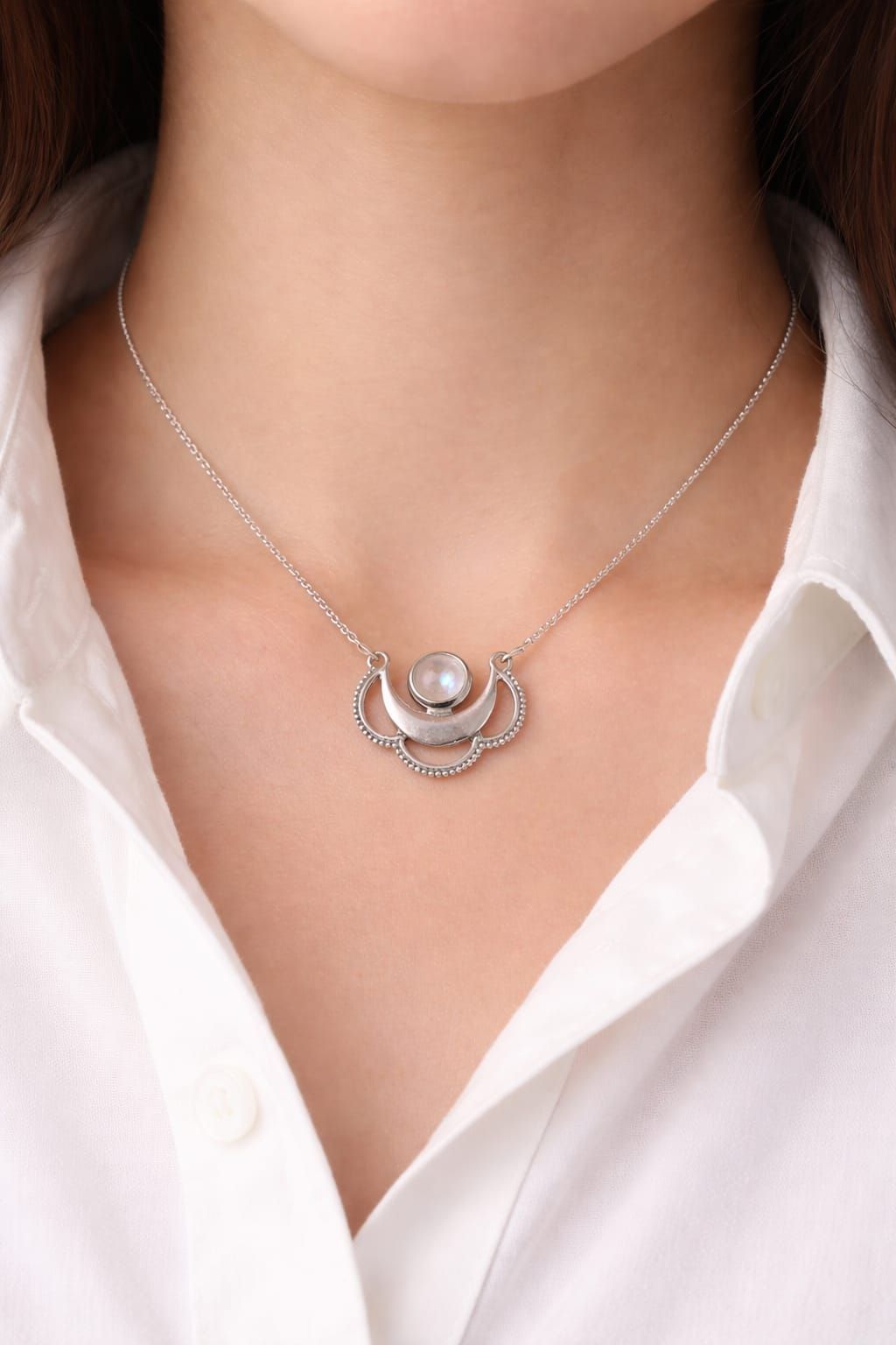 Collar de plata con colgante en forma de media luna sobre el cuello de una camisa blanca.