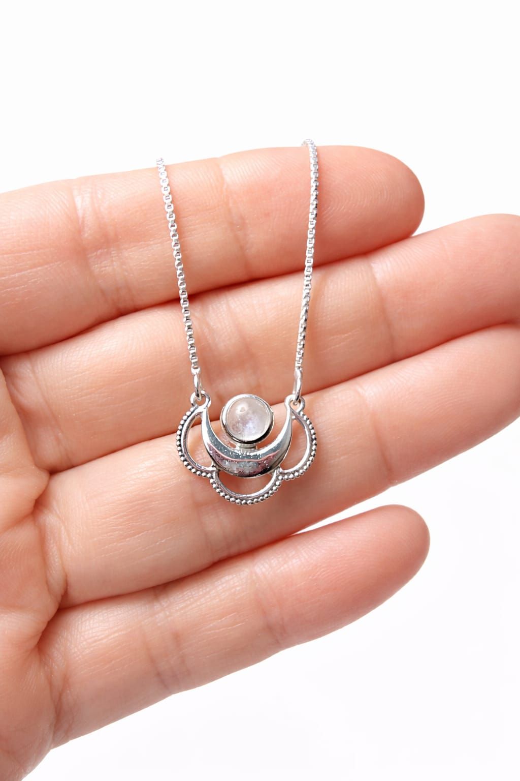 Collar de plata con colgante en forma de media luna sobre el cuello de una camisa blanca.