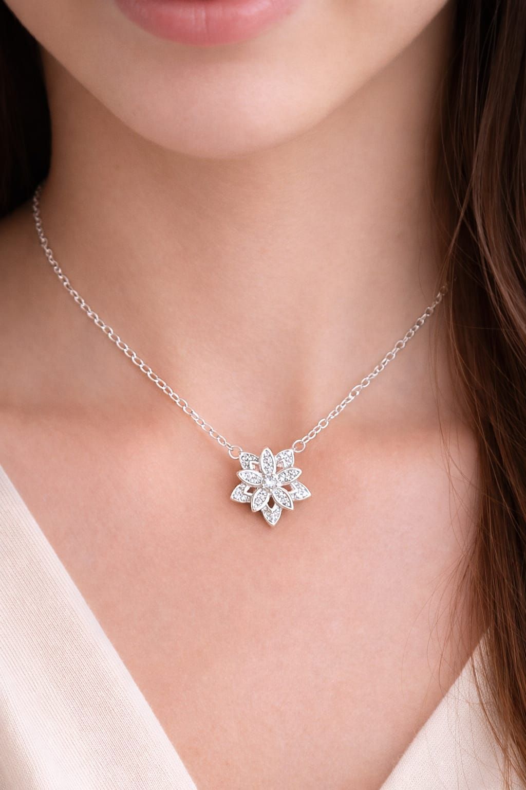 Collar con colgante de flor de plata en una delicada cadena sobre el cuello de una mujer y una blusa color crema.