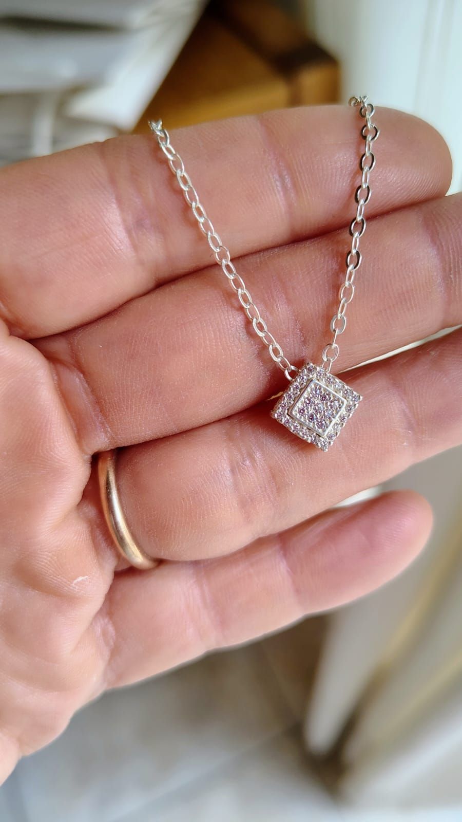 Primer plano de un collar con colgante de plata en el cuello de una mujer, que lleva una blusa blanca y cabello castaño.