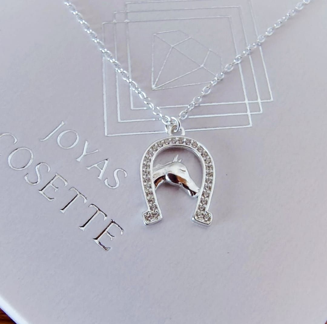 Primer plano de una persona que lleva un collar con colgante de plata sobre una blusa color crema.
