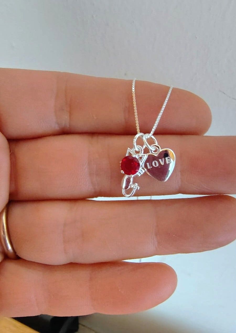 Collar de plata con colgantes de corazón y piedras preciosas rojas en el cuello y el pecho de una mujer.