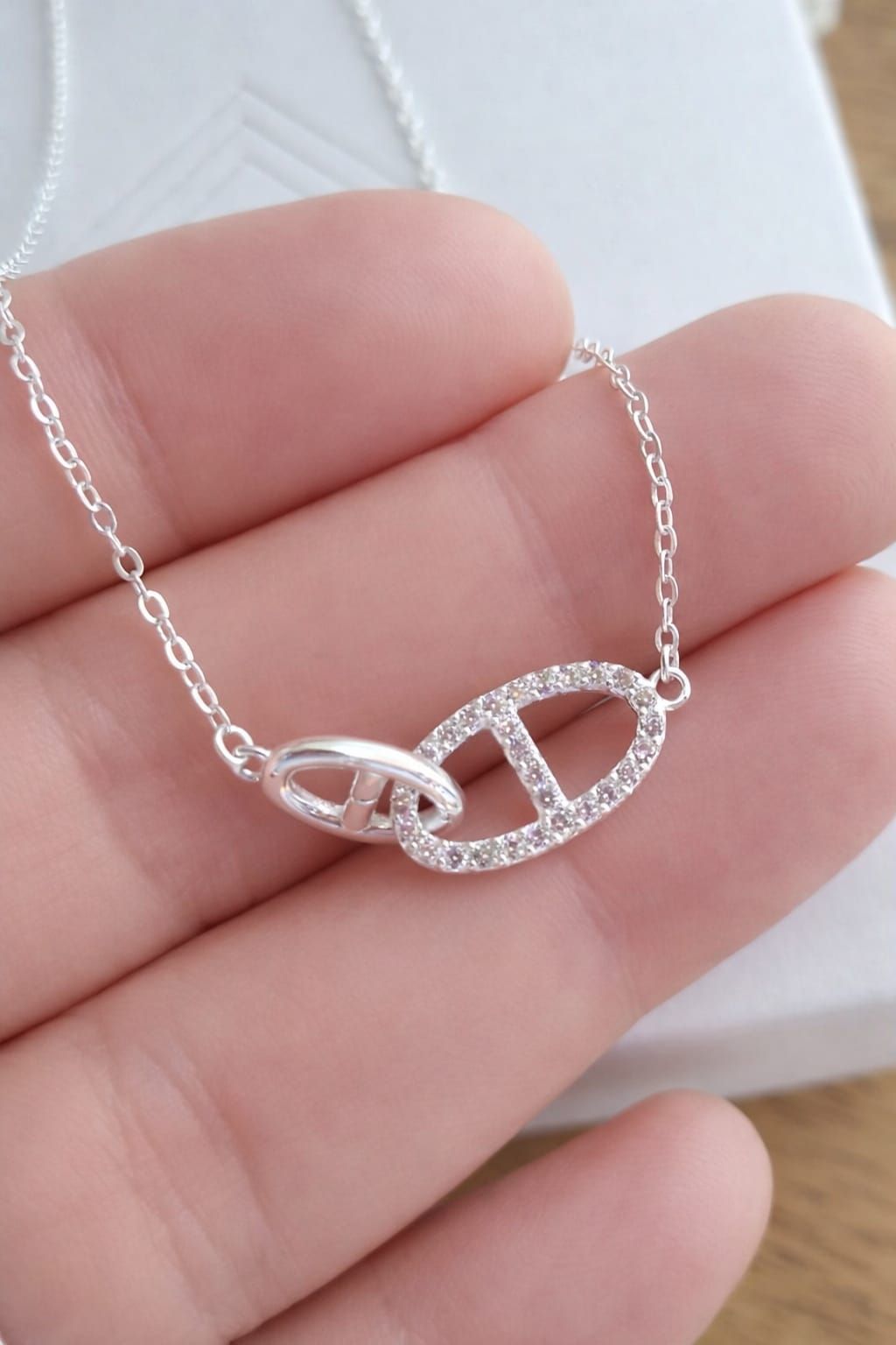Collar de plata con colgante en forma de corazón sobre el cuello de una camisa blanca.