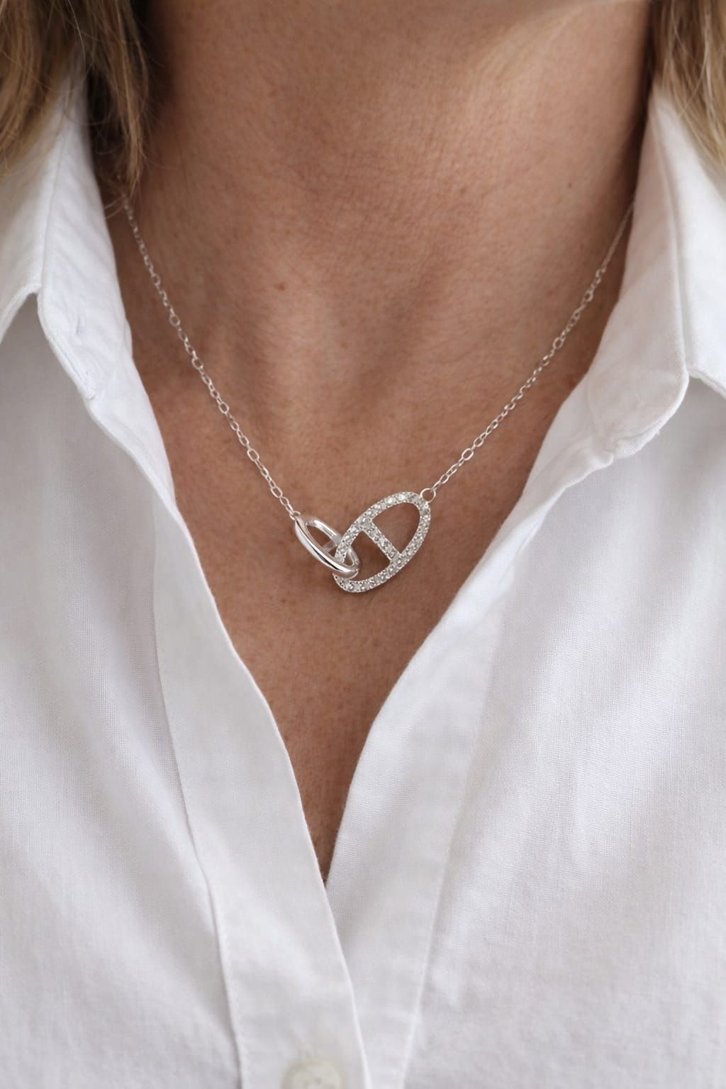 Collar de plata con colgante en forma de corazón sobre el cuello de una camisa blanca.