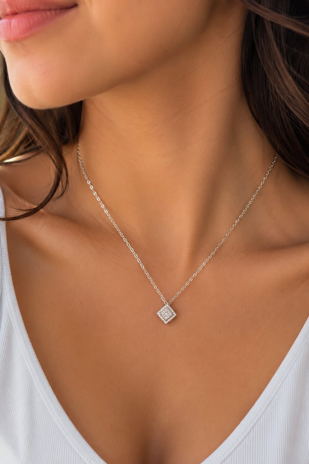 Primer plano de un collar con colgante de plata en el cuello de una mujer, que lleva una blusa blanca y cabello castaño.