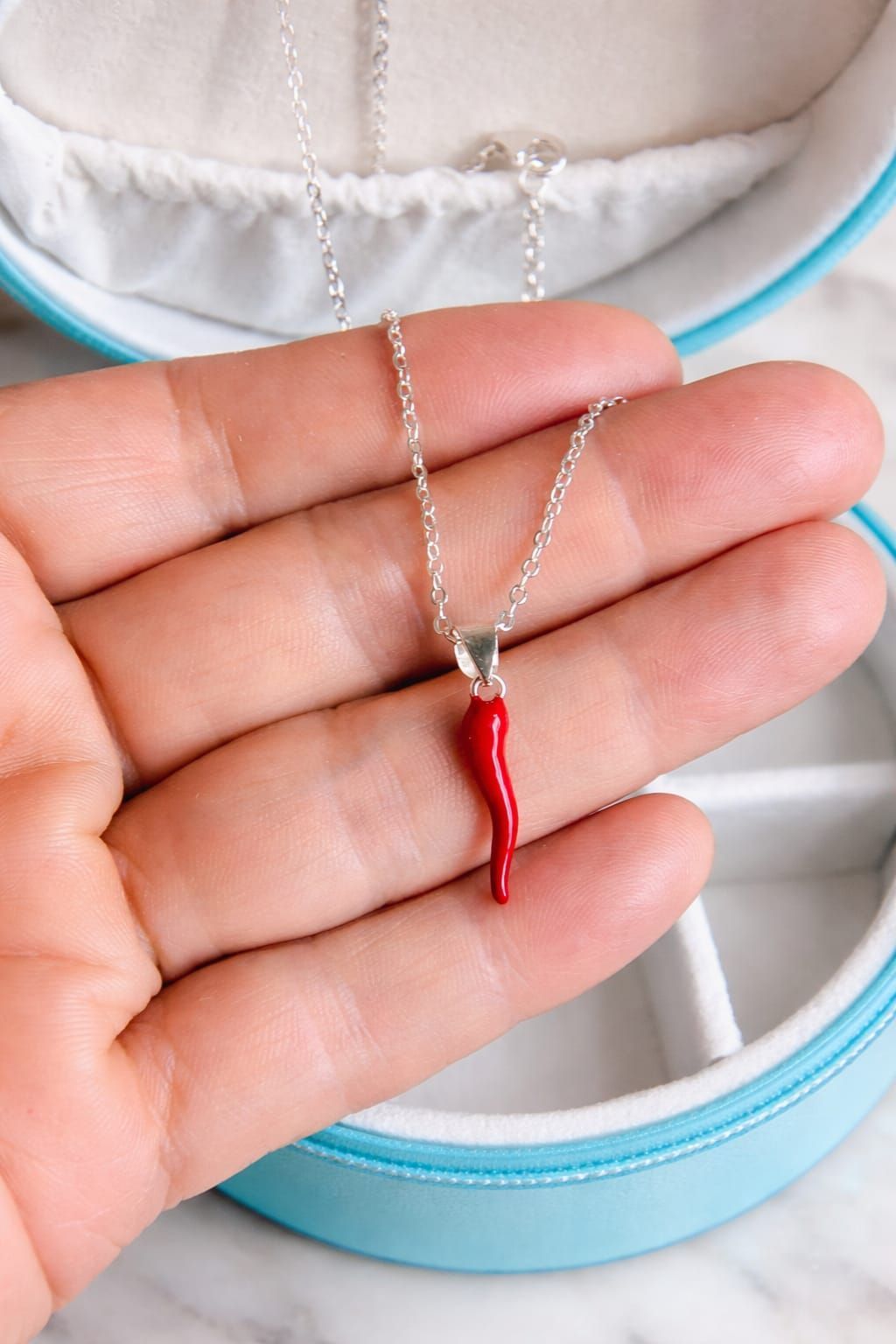 Primer plano del cuello de una camisa blanca y un collar de plata con un colgante de chile rojo.