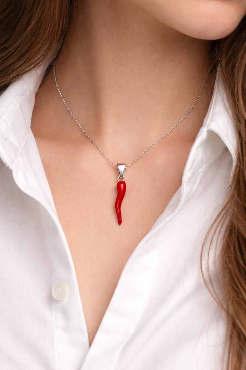 Primer plano del cuello de una camisa blanca y un collar de plata con un colgante de chile rojo.
