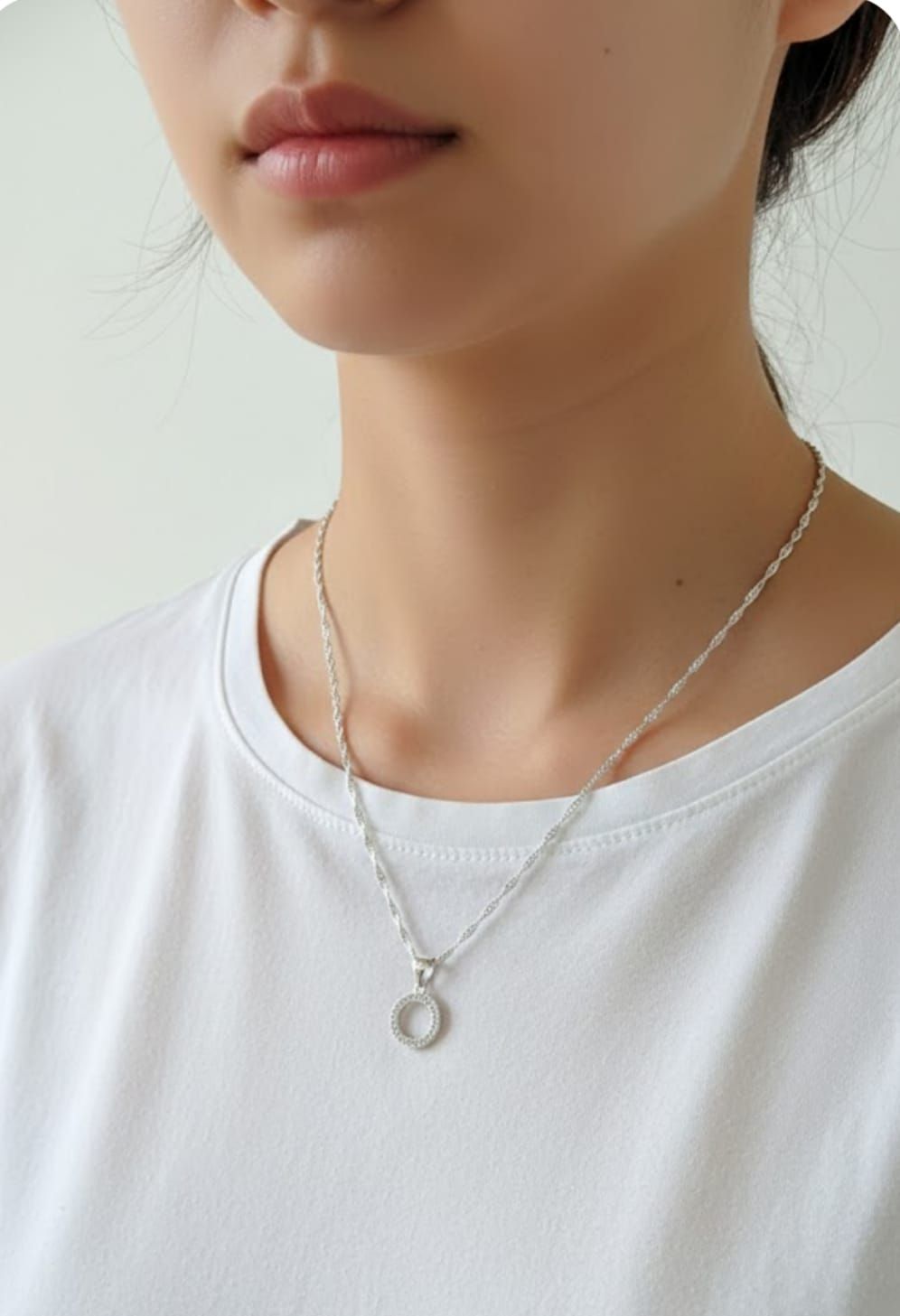 Primer plano de una persona con camisa blanca y collar con colgante plateado.