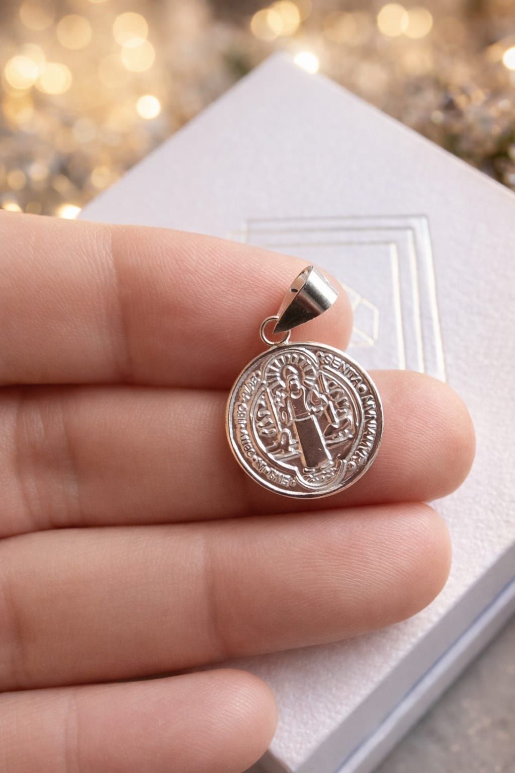 Pequeño colgante redondo de plata con un símbolo grabado, sostenido entre los dedos sobre un fondo de madera.