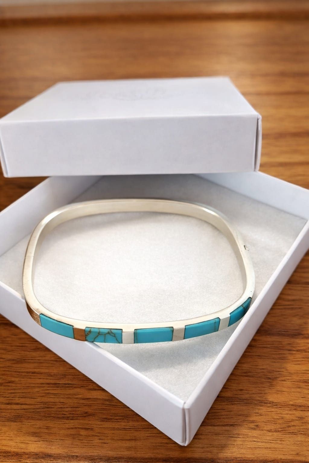 Una mano con una pulsera turquesa y plateada sobre un fondo neutro.