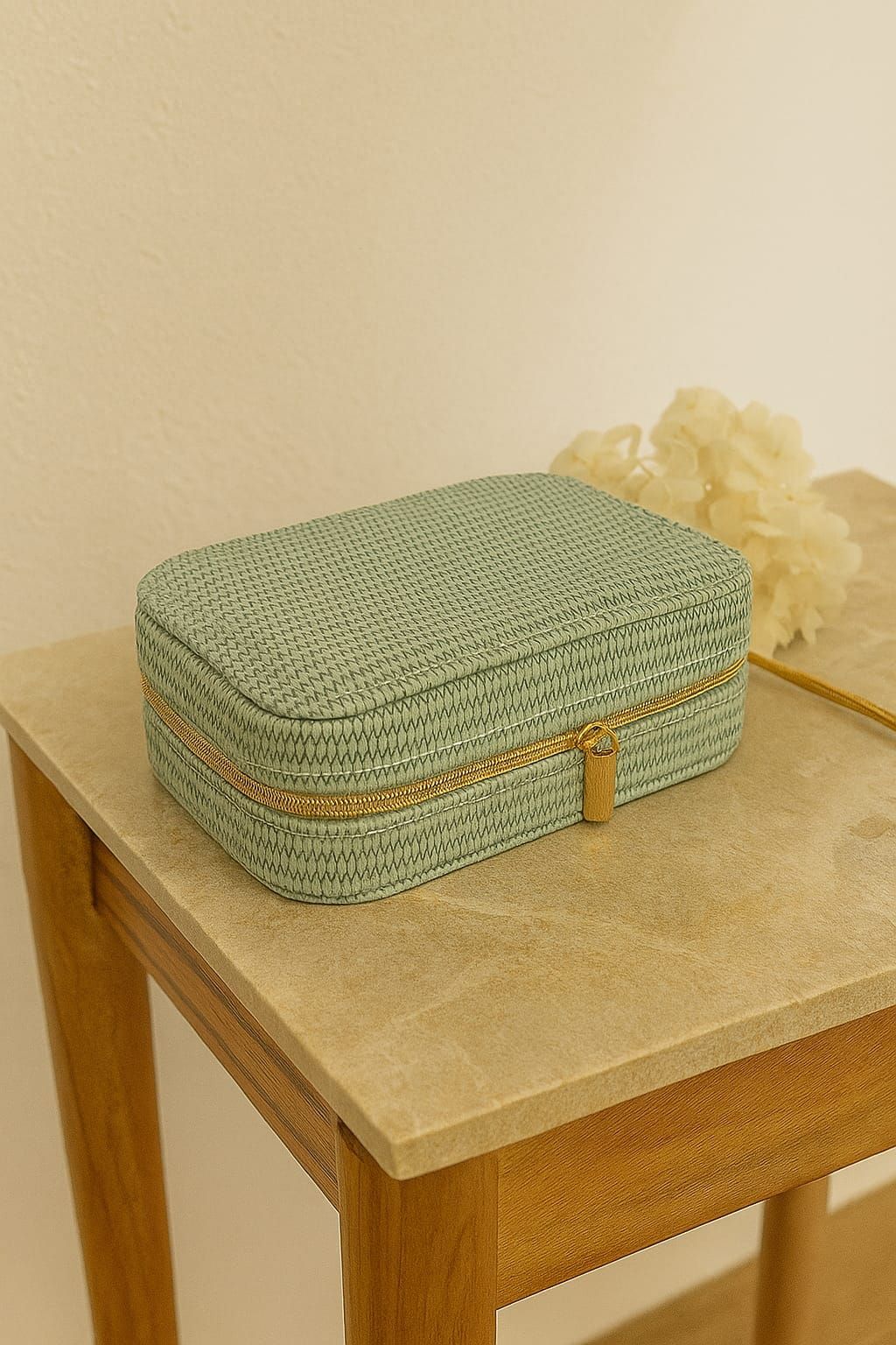Caja de almacenamiento tejida de color verde sobre una mesa de madera junto a flores pálidas.